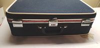Rectangular suitcase with dark blue fabric, chrome latches, black handle, and trim detailing.