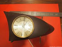 Front and top view of the Westclock shark fin clock on red background with measuring ruler showing approximate length of 11 inches and clear view of clock face.