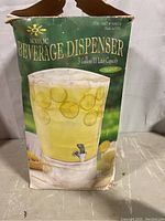 Photo of the acrylic beverage dispenser in its original packaging showing product image and branding info.