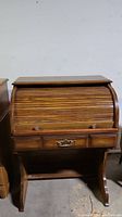 Frontal view of an antique wooden roll top desk showing the tambour closed with two side drawers and one central drawer, all with brass hardware.