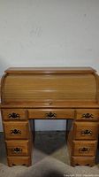Front view of closed roll top desk showing solid wood construction with multiple drawers and brass handles.