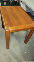 Photo showing the top and one side of the solid wood Denmark made side table with warm wood grain and rounded edges.