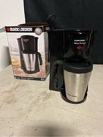 Black & Decker Brew N Go coffee maker with stainless steel travel mug and original box, shown from front.
