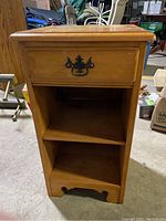 Front view of the wooden night stand showing drawer with metal handle and two open shelves.