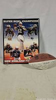 Framed New England Patriots Super Bowl 38 Champions poster with images of players and Vince Lombardi Trophy, alongside an NFL official football with visible signatures.