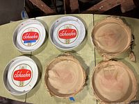 Six round Schaefer beer serving trays arranged on table, three with packaging on back, three without.