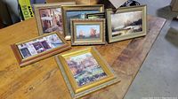 All 8 small framed wall arts arranged on a wooden surface showing various scenic pictures including boats, houses, streets, and shops.