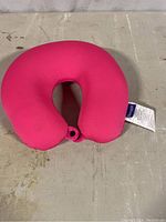 Full view of pink U-shaped travel neck pillow on concrete floor showing pillow shape and button clasp.