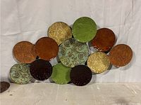 Horizontal metal wall decor with 13 colorful circular embossed discs in greens, oranges, golds, and browns