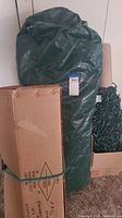 Green cover containing 7-foot artificial Christmas tree, cardboard box beside it likely containing accessories.