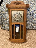 Full frontal view of the antique wooden wall clock showing carved wood details and metal clock face with Arabic numerals.