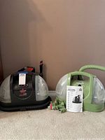 Two Bissell Auto Care ProHeat spot cleaners side by side on carpeted floor, including attachments and manual.