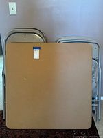 Photo of the square vinyl top card table with scratches, showing brown surface and dark legs with a label sticker on the table edge.