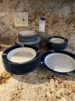 Stacked assorted plates and bowls with a blue border and white floral design on a granite counter.