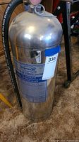 Photo showing side view of vintage metal fire extinguisher with hose and label indicating operational instructions and brand General.