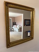 Front view showing rectangular mirror with gold decorative trim reflecting a living room.