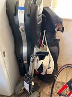 Hard golf bag suitcase, a set of golf clubs in a soft golf bag, and parts of a golf caddy visible alongside them.