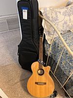 Full view of Epiphone acoustic-electric guitar leaning against bed with gig bag