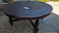 Full side view showing the round etched leather tabletop with visible scratches and the turned wooden legs supporting the table.