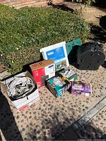 Overview photo showing the boxed tripod mount, coiled cables in a box, a boxed security light, and other accessories arranged outdoors on a pebble patio.