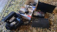 Full lot view showing multiple keyboards, video transfer system box, camcorder with case, tire inflator, assorted cables and adapters on carpet.