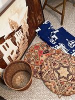 Overall view of the lot showing framed painting, basket, woven table pads, and folded blue table scarves.