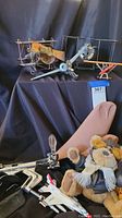 Several decorative model planes on black cloth backdrop along with a stuffed bear toy and wine bottle opener visible.