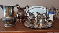Group showing all items including several silver pitchers, a tea set on a tray, and a large tray behind.