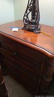 Image of dresser corner showing wood finish and drawer design with lamp base on top.
