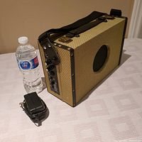 Beaver Creek BCAMP-5A amplifier with power adapter and water bottle for scale, showing textured tan exterior and panel controls.