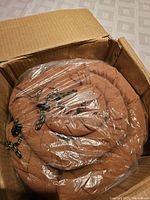 Mattress rolled up in brown color secured with ties inside plastic, partially inside original cardboard box.
