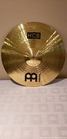 Front view of bright, shiny metallic ride cymbal with visible grooves and Meinl and HCS logo prints.