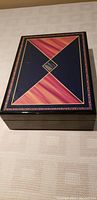 Closed inlaid wooden box with dark blue and reddish-brown inlaid pattern accented with gold lines.