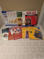 Photo showing an array of photographic papers including Epson glossy, matte, and premium plus; Staples heavy matte; Kodak picture papers; and HP sticker project and sketchpad papers.