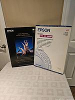 Two boxes of Epson large format photo paper; front view showing the box of Ultra Premium Photo Paper Luster and box of Ink Jet Paper A2 size