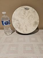 Front view of the 10 inch Remo Fiberskyn hand drum next to a water bottle for size reference.