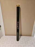 Full length black cylindrical rod case standing upright with Orvis logo and brass-like metal closure visible.