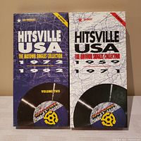 Two CD box sets standing upright showing front covers with map backgrounds and vinyl record graphics. Volume one covers 1959-1971, volume two covers 1972-1992.