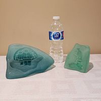 Two green Inuit etched glass sculptures displayed next to a water bottle for scale, showing their varying sizes and shapes.