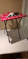 Folding snack table showing red maple leaf-shaped top with Team Canada hockey player logo and 'CANADA' text.