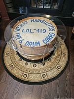 Top view of coffee table showing clear bevelled glass top on antique Wesley Marvelettes bass drum with blue text on drum head, sitting on patterned round area rug.