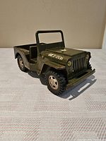 Front left angle view of vintage army green Tonka toy jeep, showing detailed front grille, headlights, windshield frame, tires and hood.