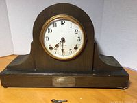 Full view of the dark wooden Sessions mantle clock with brass bezel, white dial and inscription plaque on base, showing key placed in front.