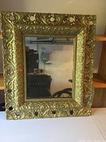 Front view of the ornate gold mirror showing the detailed decorative frame with circular cutouts and floral scrollwork.