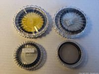 Four camera filters in plastic protective cases arranged on a flat surface showing differences in tint and sizes.
