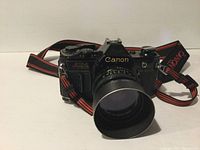 Front-facing view of Canon AE-1 body with mounted 50mm lens and hood, strap laid behind