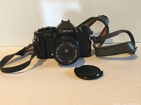 Front view of Canon F-1 body with attached lens and strap laid flat, lens cap in foreground