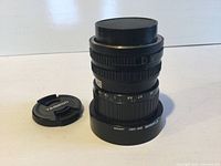 Canon zoom lens 35-70mm with macro function, front Tamron lens cap beside it, photographed from a slight angle showing front markings and lens body