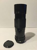 Front view of Canon 70-150mm zoom lens with lens cap next to it on the left. Lens barrel shows aperture markings (f1.5, 1.7, 2).