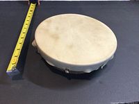 First handmade First Nation drum with tape measure showing approx 8 inch diameter and natural hide drumhead with traditional handle visible on side.